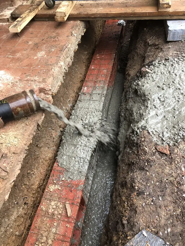Concrete being poured into a brick-lined foundation trench