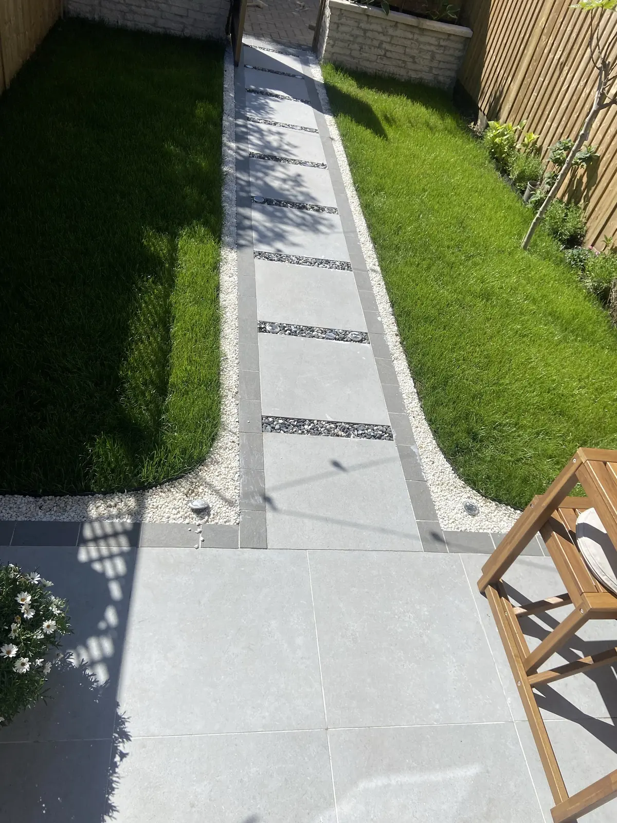 Long pale paved garden path with inset strips running between two lawns