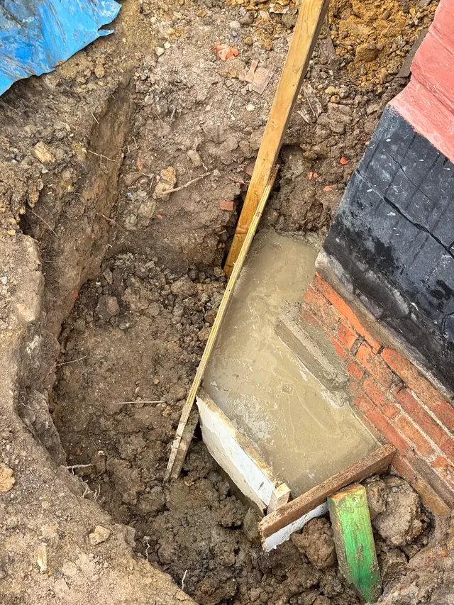 New concrete poured beneath an existing foundation in an excavated trench
